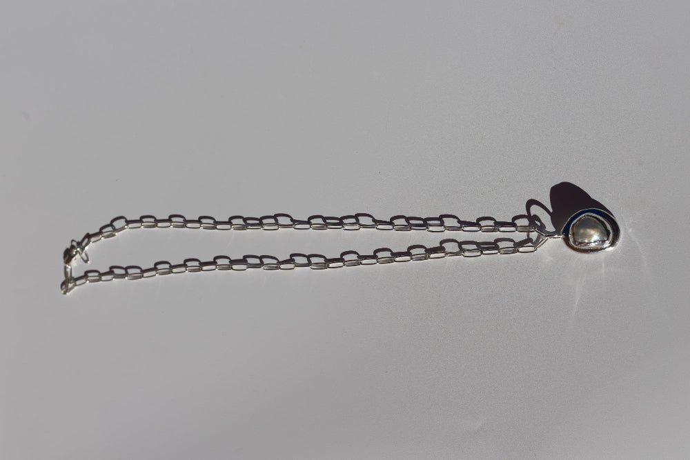 A silver-toned metal chain accessory with a small heart-shaped pendant, photographed on a plain light gray background.